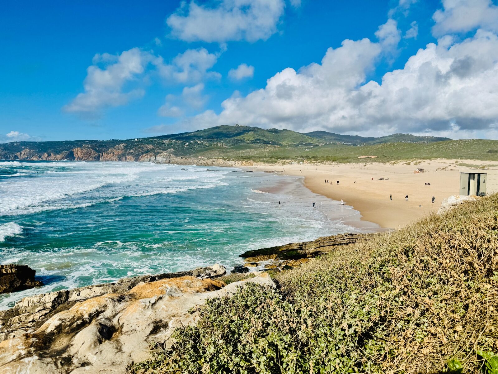 Guincho beach, Cascais — turquoise Atlantic waves rolling onto a long stretch of golden sand with the Sintra hills behind