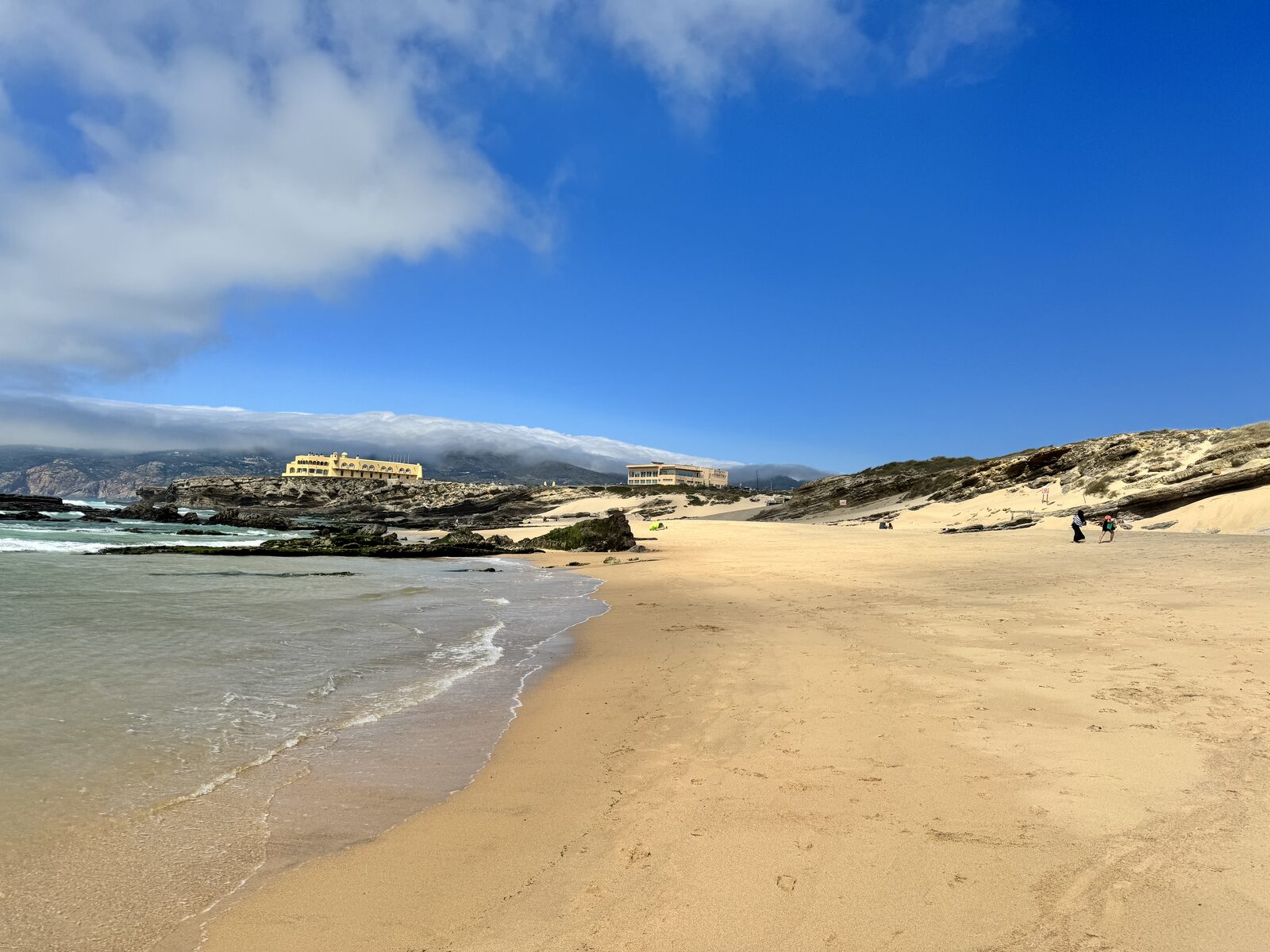 A quiet stretch of beach near Cascais with soft morning light, calm shoreline and a low ridge of cliffs in the distance