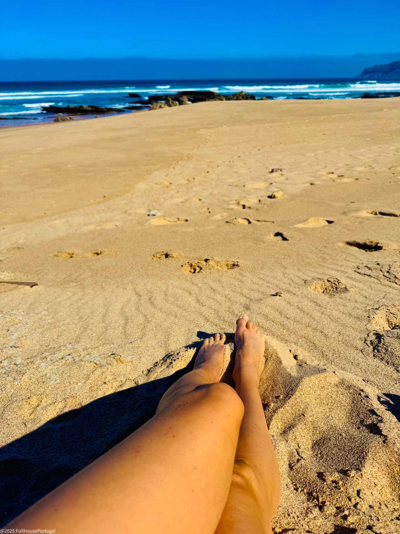 Sun-drenched beach on the Cascais coast with rolling Atlantic waves and footprints in the sand