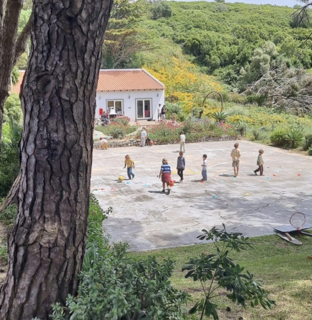 Children playing on the courtyard at Villora Academy in Malveira da Serra, with the main building and pine trees in the background